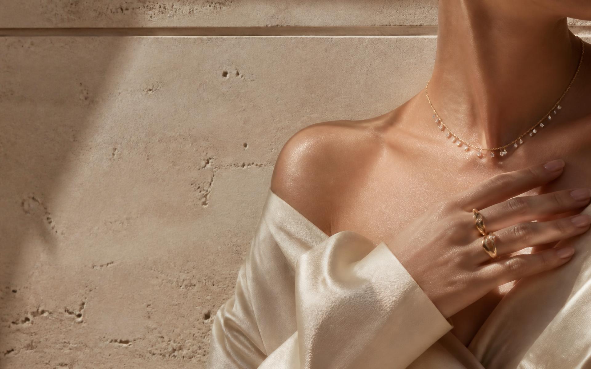 Fine gold and diamond jewelry worn against a warm travertine wall